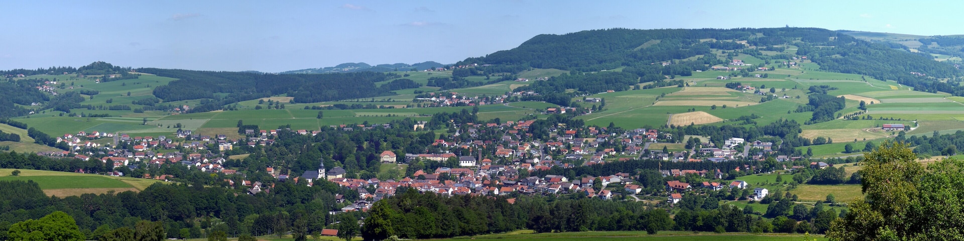 Gersfeld (Rhön), auf etwa 400 Meter über Normal Null gelegen, ist eine als Luftkurort und Kneipp-Heilbad anerkannte Stadt inmitten der hessischen Rhön. Rechts oben die Wasserkuppe mit Radarkuppel, mit einer Höhe von 950 Meter höchster Berg der Rhön. Links oben der 705 Meter hohe Wachtküppel. Mitte oben das Fuldaer Haus vor der 706 Meter hohen Maulkuppe.
