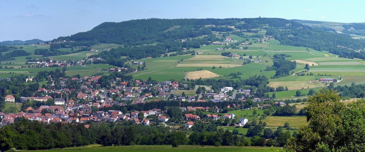 A rural town nestled in rolling hills with fields and scattered houses.