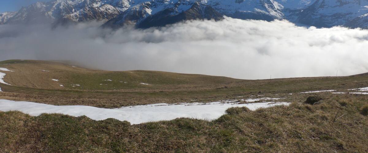 A mountain range with snow-covered peaks and a valley with patches of snow and grass.