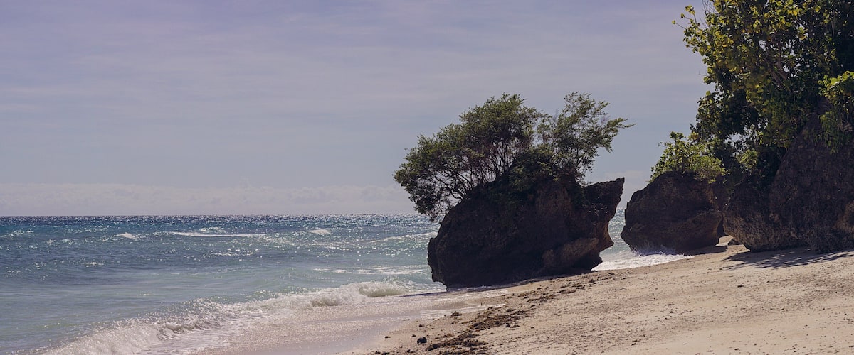 A beach with clear blue water, sandy shore, and large rock formations.
