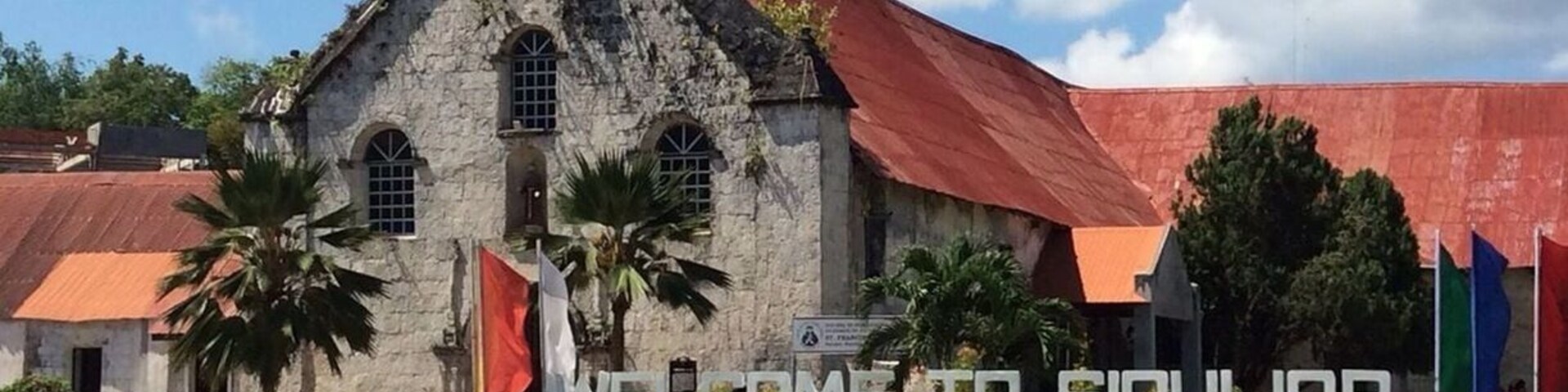 Una iglesia con techo rojo y una cruz en la parte superior. Hay un letrero de bienvenida frente a la iglesia.