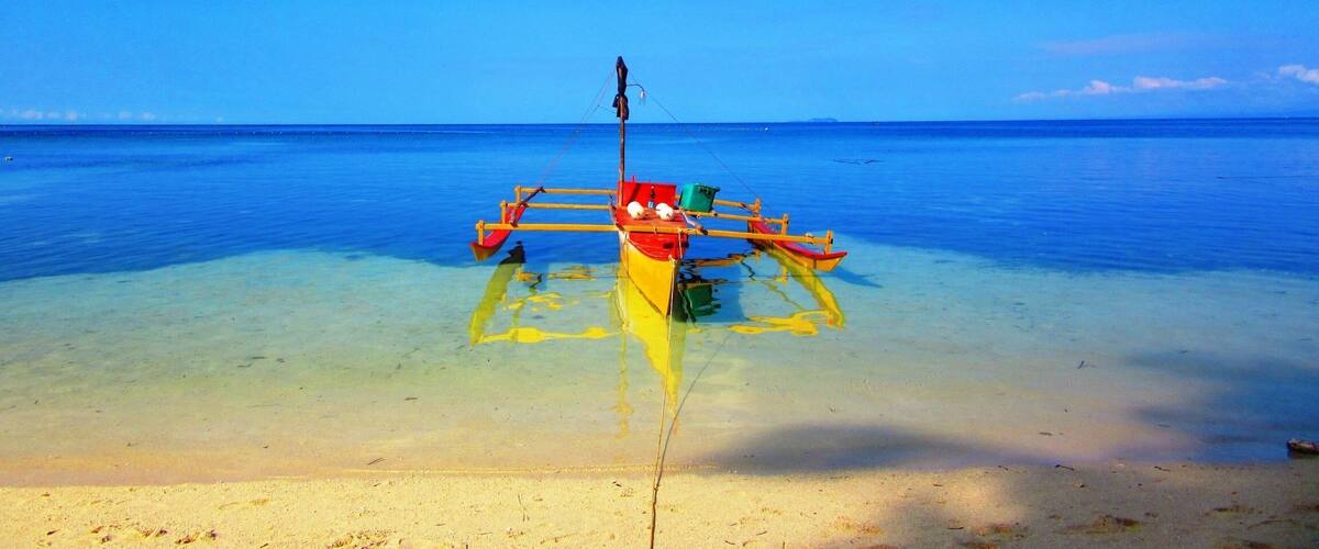 A clear blue sky, calm sea, and a boat with a fishing net on a sandy beach.