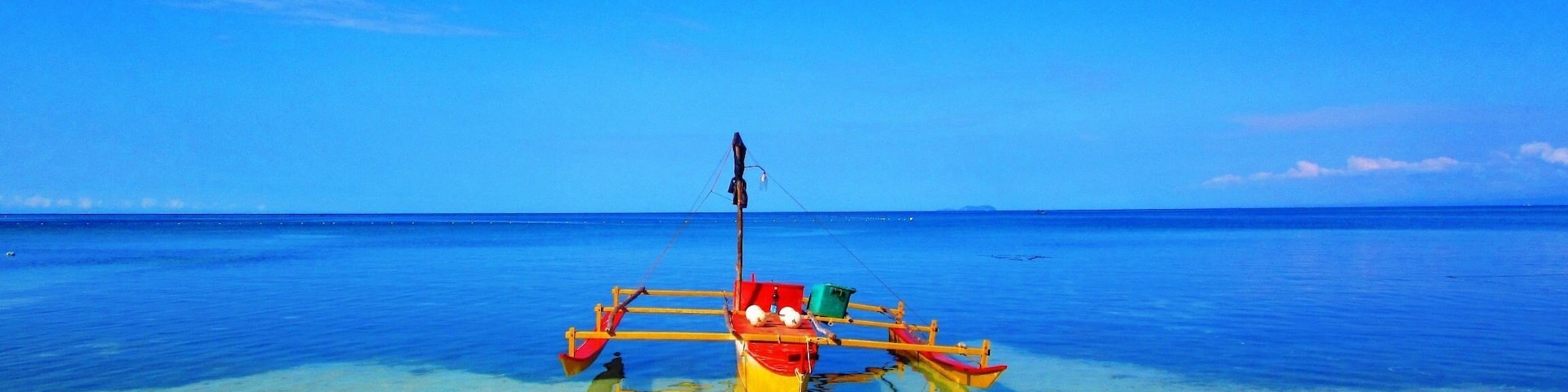 A clear blue sky, calm sea, and a boat with a fishing net on a sandy beach.