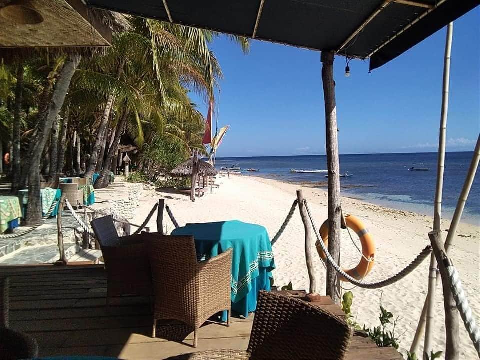 A beachside restaurant with wicker furniture and a blue tablecloth, overlooking the ocean.