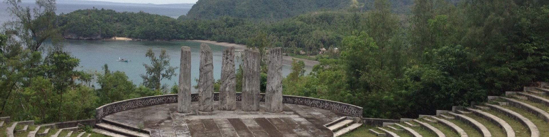 An amphitheater with a circular stage surrounded by tiered seating, overlooking a lake and forested hills.