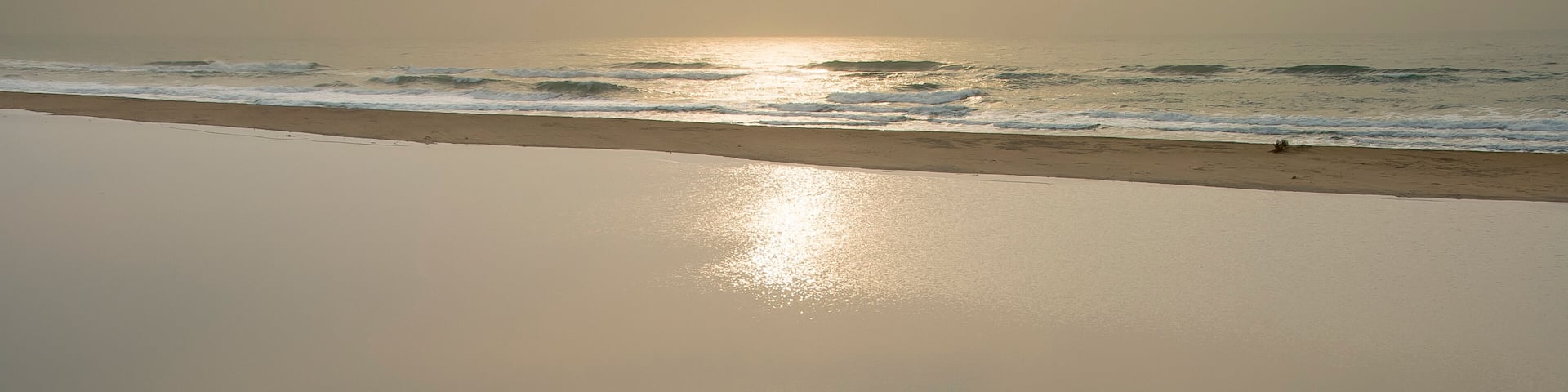 A beach with calm waves and a clear reflection of the sun on the water.
