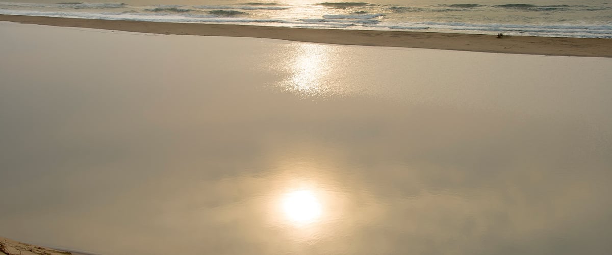 A beach with calm waves and a clear reflection of the sun on the water.