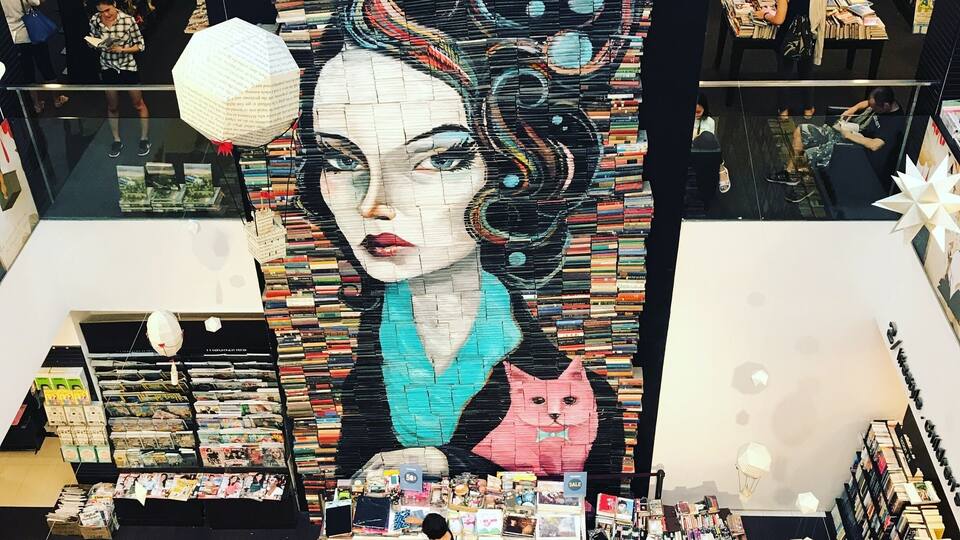 A bookstore with a large mural of a woman and a cat, surrounded by bookshelves and a checkout counter.