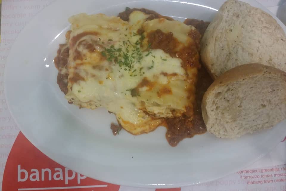 A plate with a baked dish topped with cheese and herbs, accompanied by two pieces of bread.