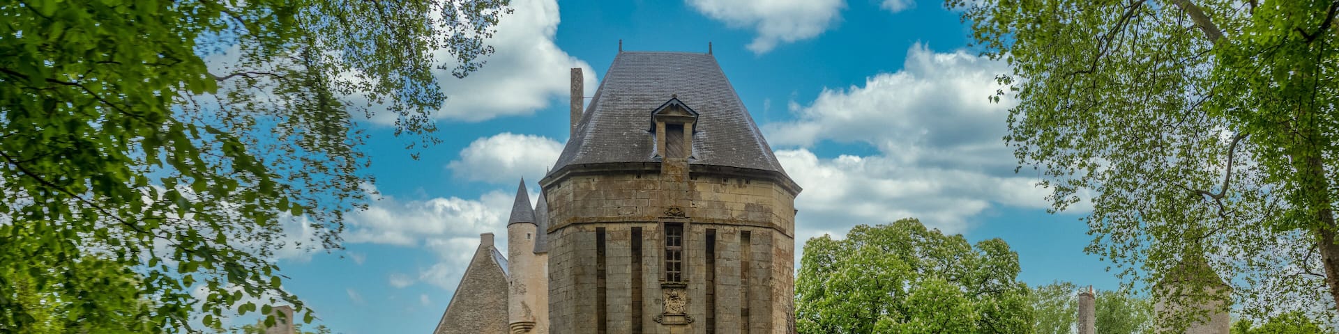View of historic monument Bannegon castle in France with large intact gate tower, wooden draw bridge over the water filled moat, imposing keep, drawbridge, and a trapezoidal fortified enclosure