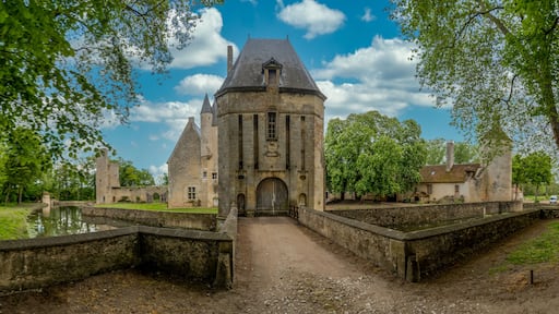 View of historic monument Bannegon castle in France with large intact gate tower, wooden draw bridge over the water filled moat, imposing keep, drawbridge, and a trapezoidal fortified enclosure