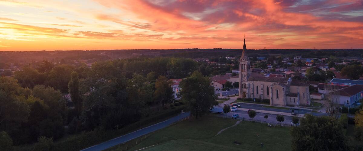 A church with a tall steeple, surrounded by trees and a town in the background.
