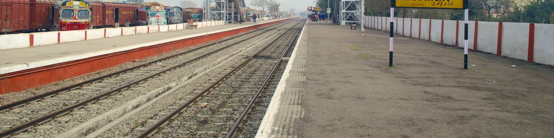 A railway station platform with multiple tracks, a pedestrian overpass, and a sign indicating 'RUDRAPUR CITY'.