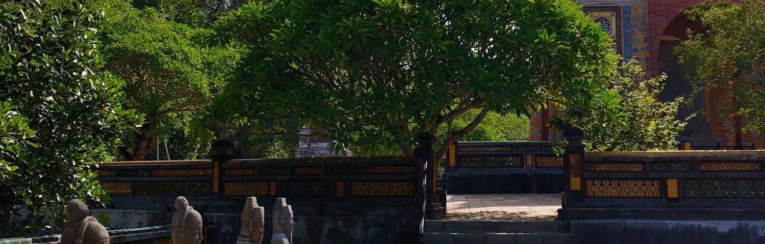 Pátio com estátuas de pedra, uma grande árvore e um edifício tradicional ao fundo.