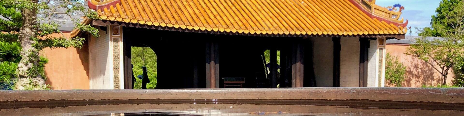 A traditional building with a tiled roof and a reflection in the water in front.