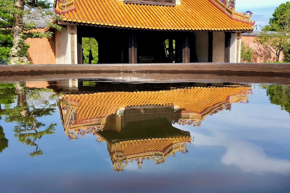 Un edificio tradizionale con tetto in tegole e il suo riflesso nell'acqua davanti.