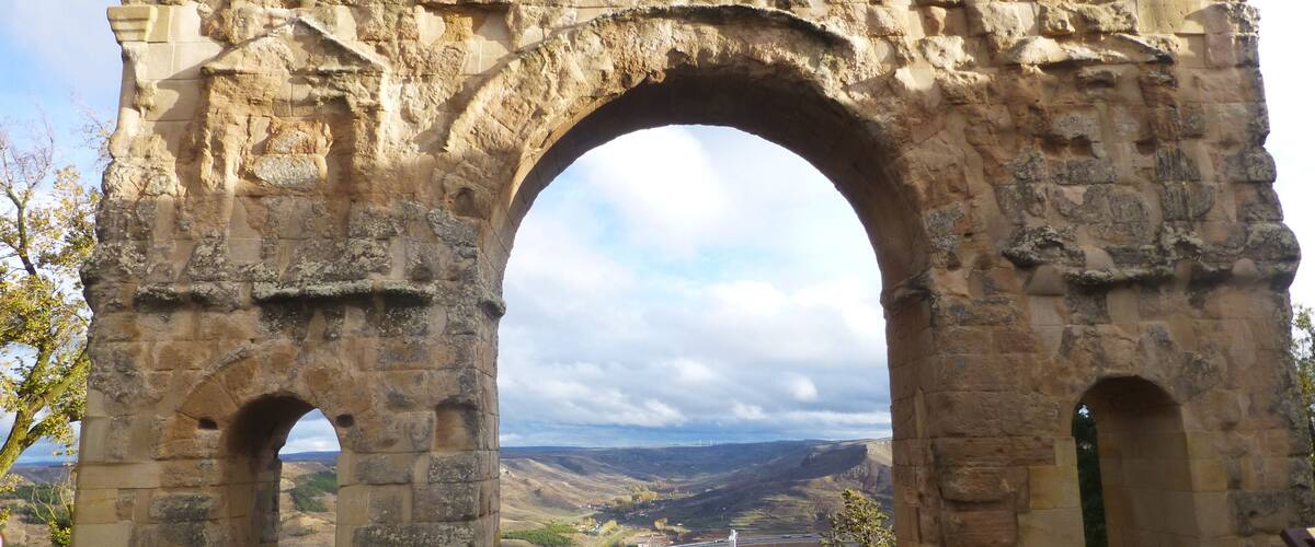 An ancient stone archway with a view of a valley and distant mountains.