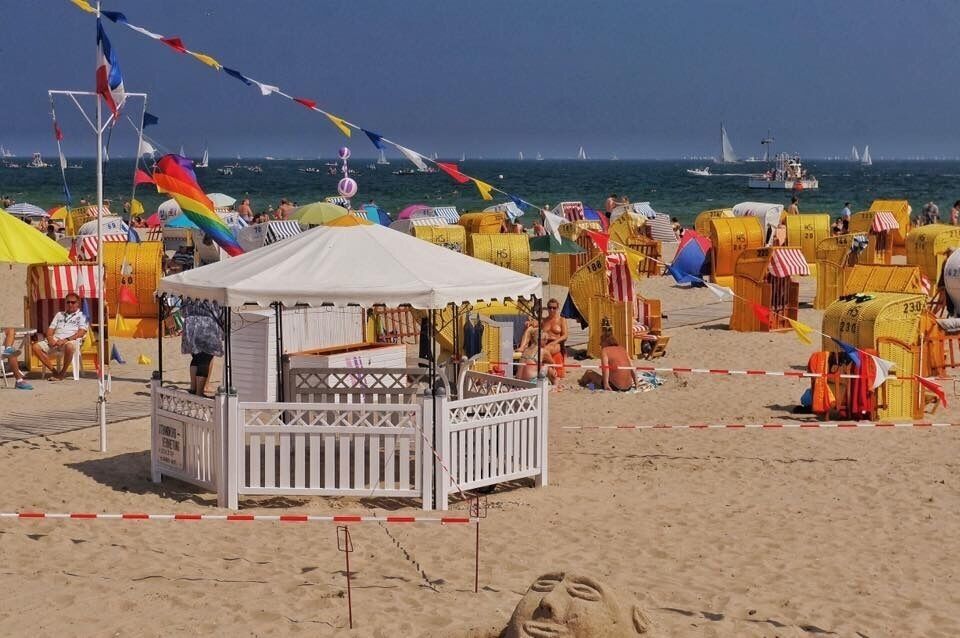 A crowded beach with colorful beach huts and a white kiosk.
