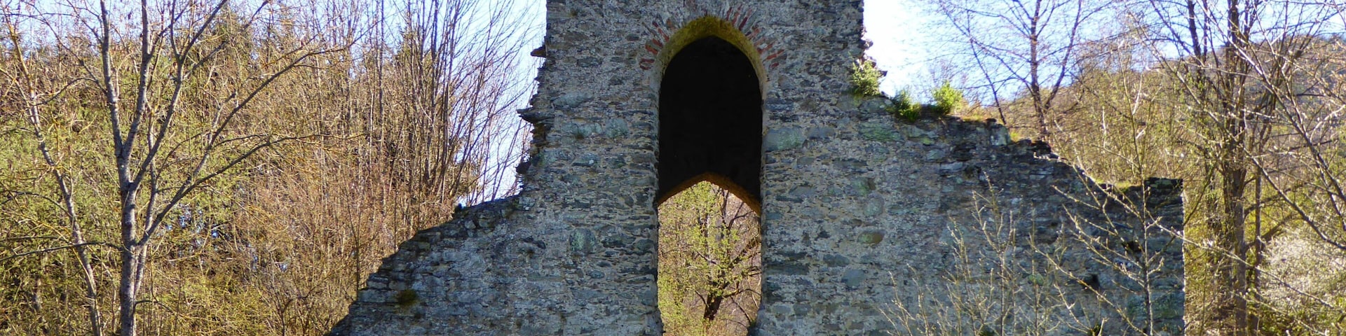 Ruinas de piedra con un gran arco, rodeado de árboles y césped.