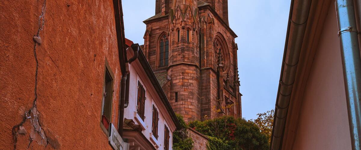 A cobblestone street leading to a tall, ornate church with a spire.