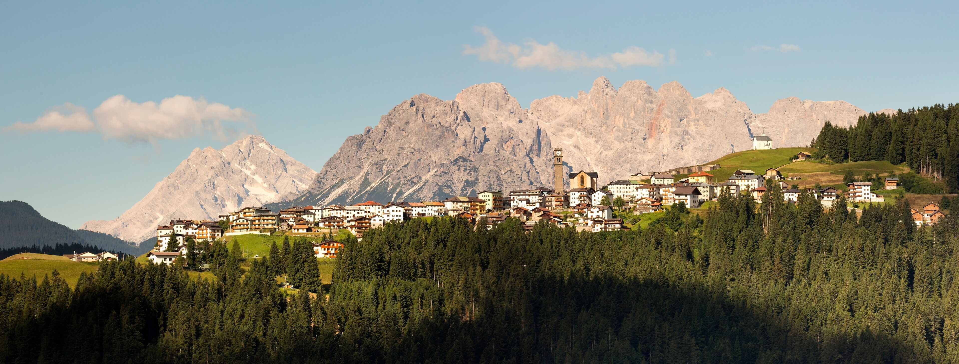A mountain village with buildings nestled among pine trees and a backdrop of rugged mountains.