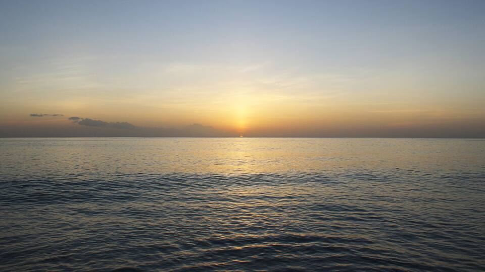 A calm sea at sunset with a clear sky.