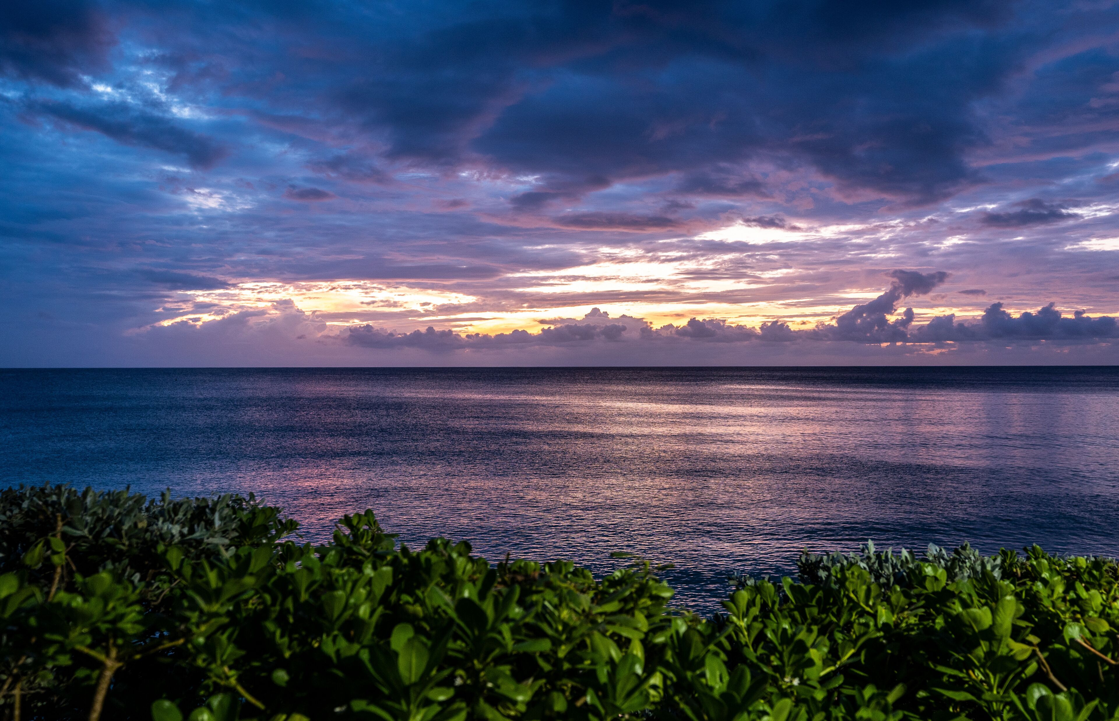 A sunset over the ocean with a clear sky and calm waters.