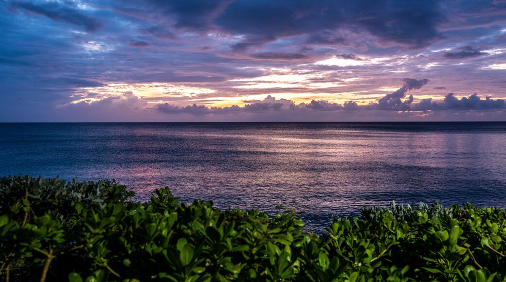 A sunset over the ocean with a clear sky and calm waters.
