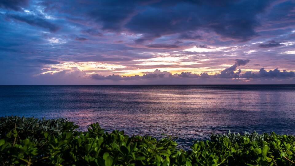 A sunset over the ocean with a clear sky and calm waters.