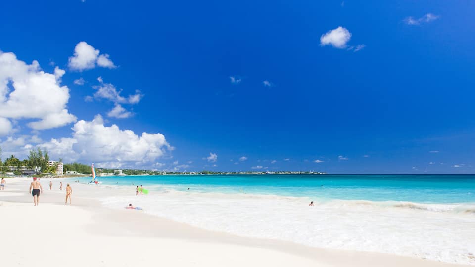 A beach with clear turquoise water, white sand, and a few people enjoying the sun.
