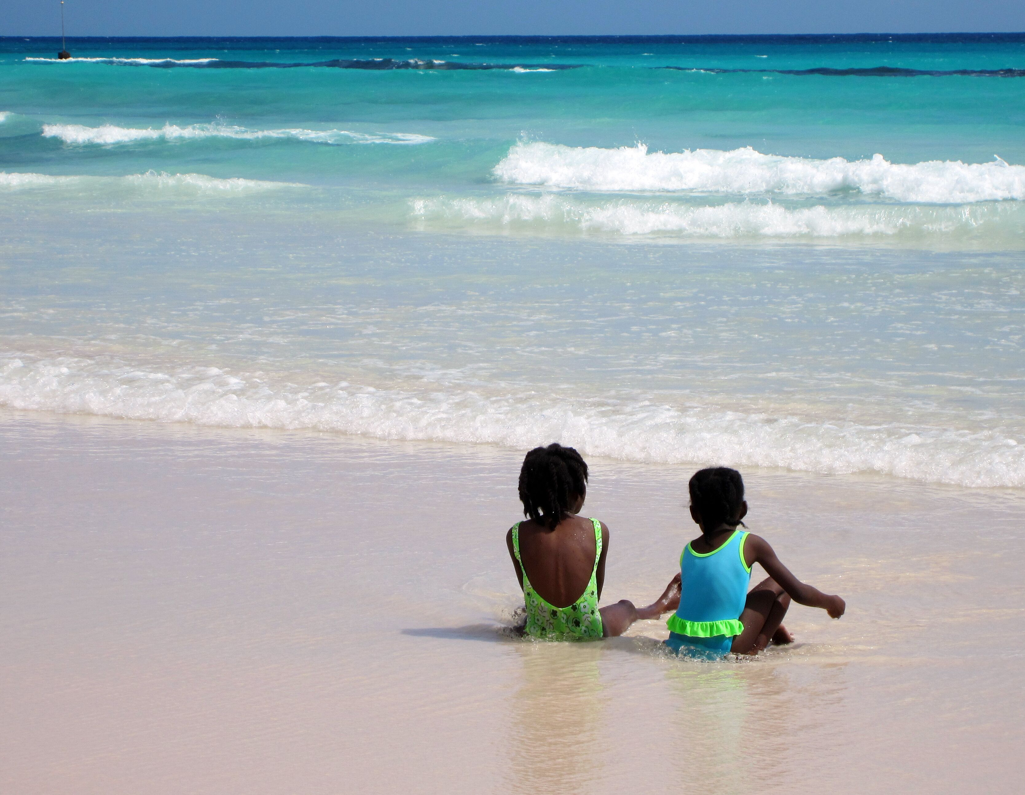 Dos niños jugando en una playa arenosa con olas turquesas del océano.