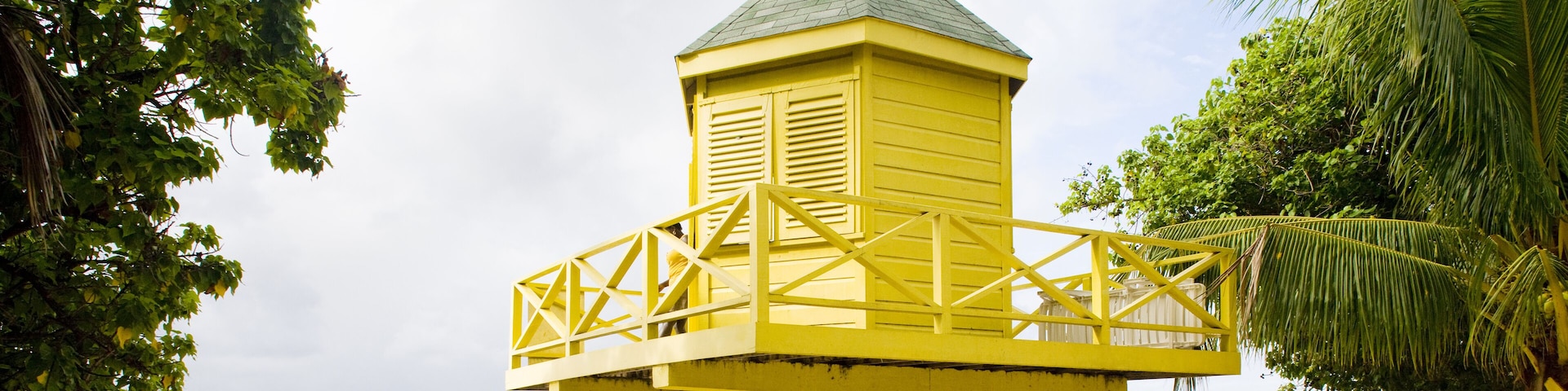 Uma torre amarela de salva-vidas numa praia arenosa com água azul cristalina e palmeiras.