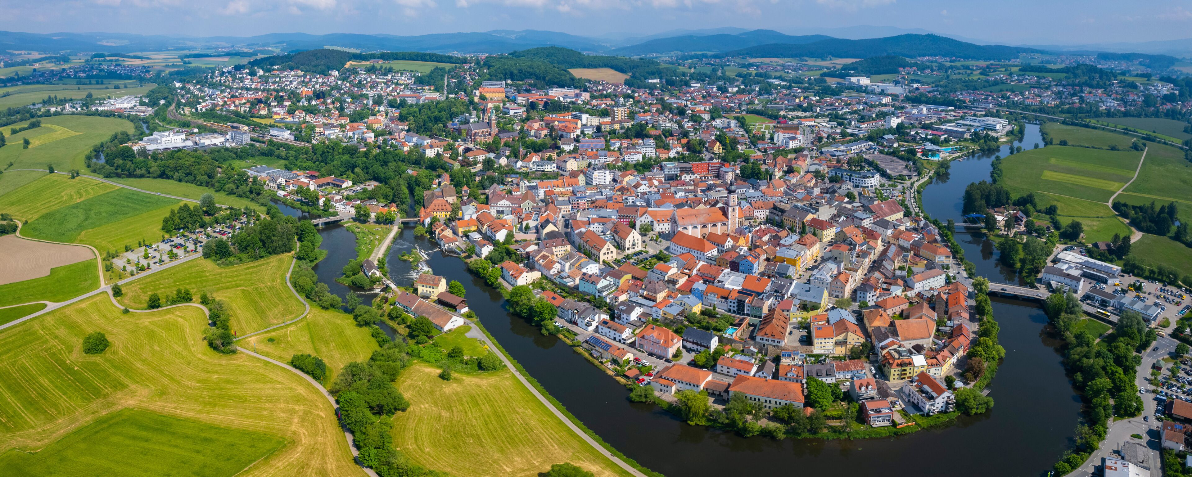 A river winding through a densely packed town with red-roofed buildings and green fields on the outskirts.