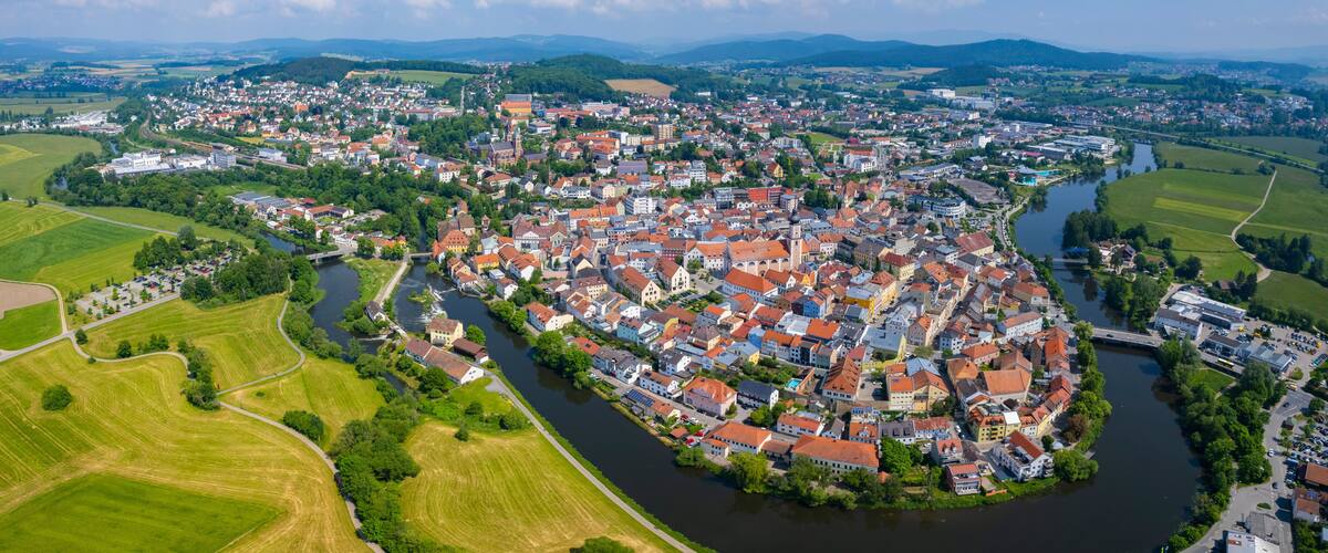 A river winding through a densely packed town with red-roofed buildings and green fields on the outskirts.