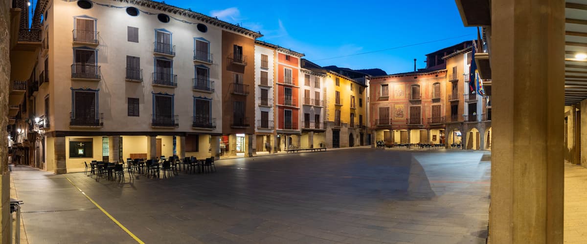 A plaza with historic buildings, outdoor seating, and a clear sky.
