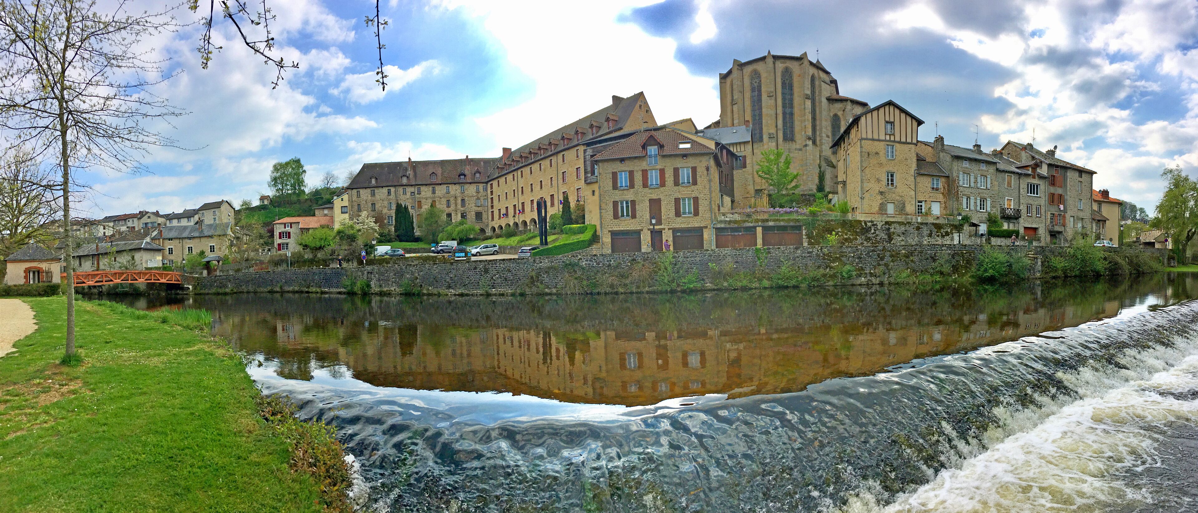 A historic building complex by a river with a small waterfall.