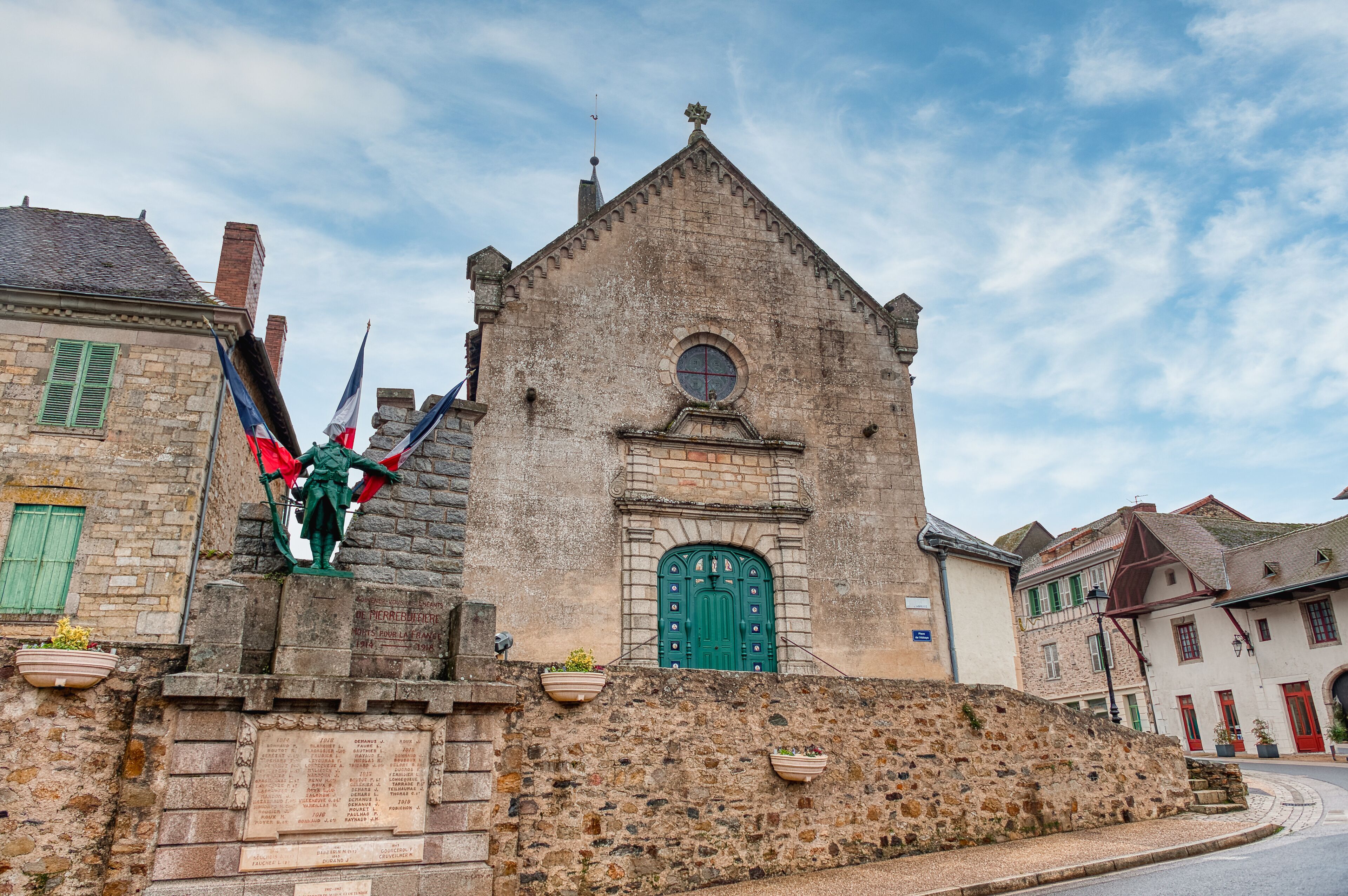 A historic stone church with a green door, a statue of a knight, and a stone wall with plaques.