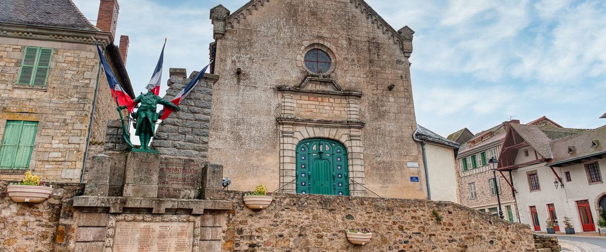 A historic stone church with a green door, a statue of a knight, and a stone wall with plaques.