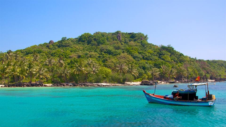 A boat on turquoise water, a small island with dense green vegetation, and a clear blue sky.