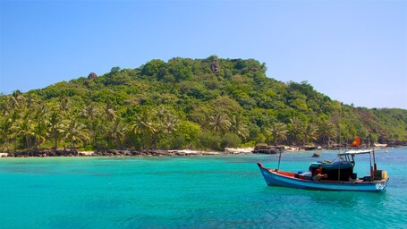 Ein Boot auf türkisblauem Wasser, eine kleine Insel mit üppiger grüner Vegetation und einem wolkenlosen, blauen Himmel.