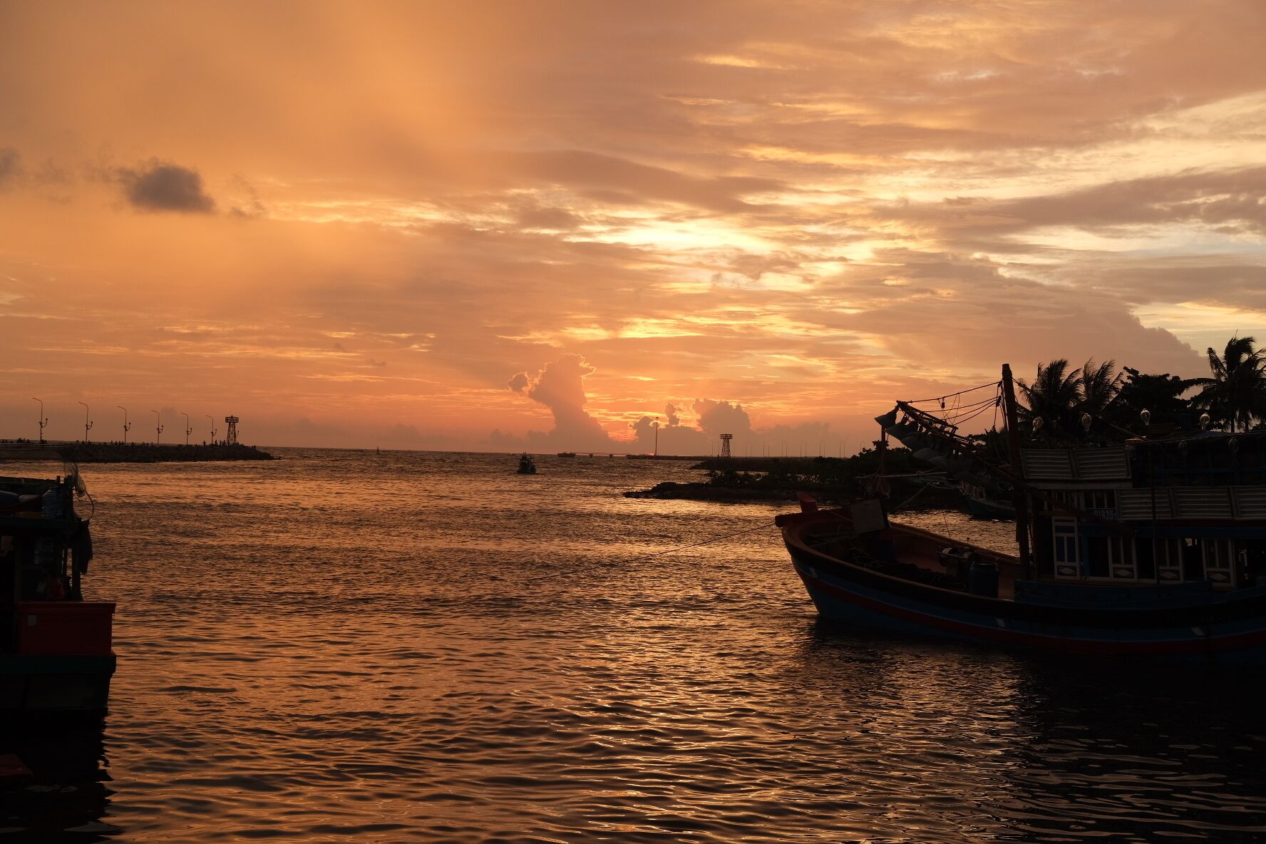 A sunset over a calm sea with boats and a distant island.