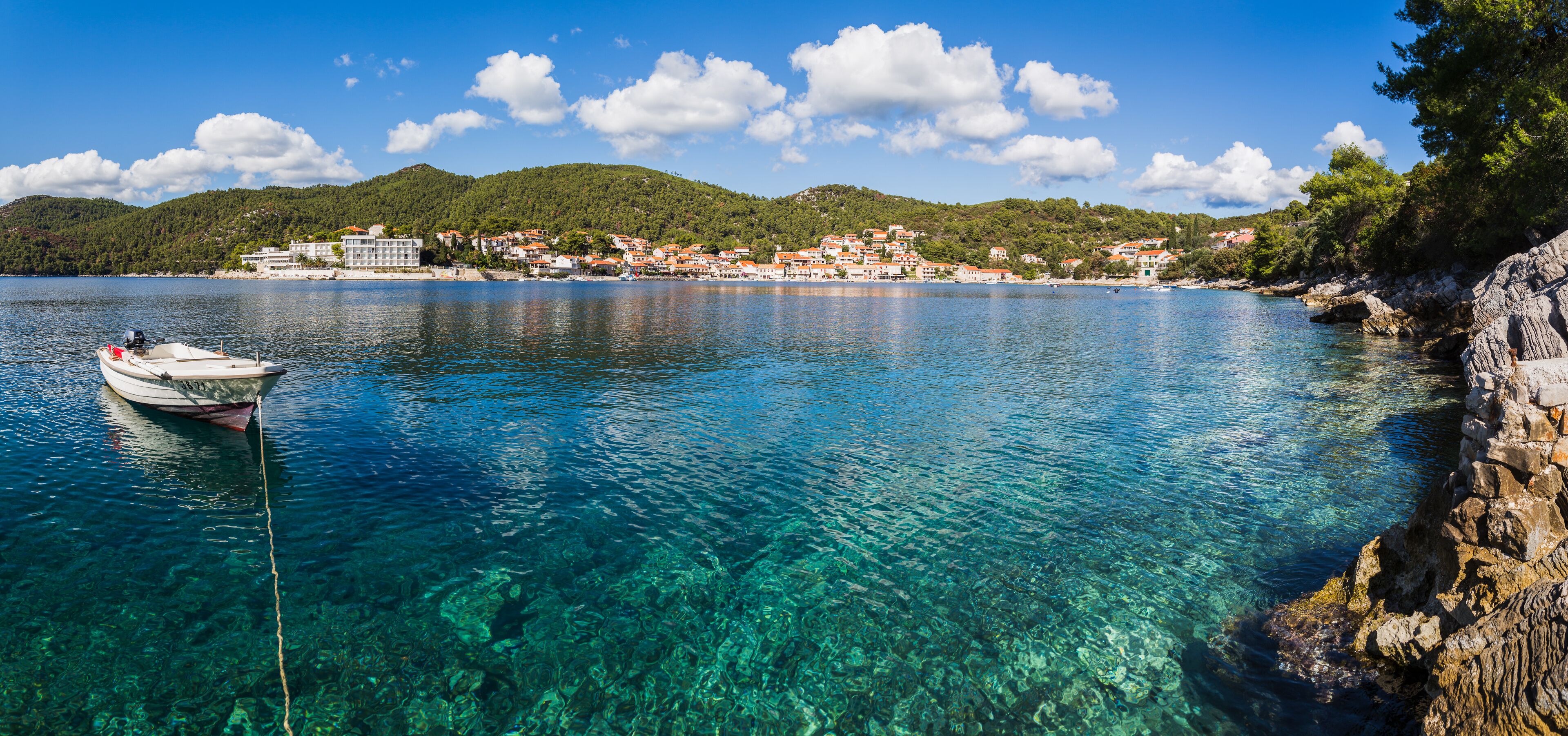 A clear blue lake with a boat anchored on the left, surrounded by rocky shores and a town with buildings on the right.