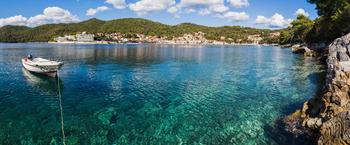 A clear blue lake with a boat anchored on the left, surrounded by rocky shores and a town with buildings on the right.