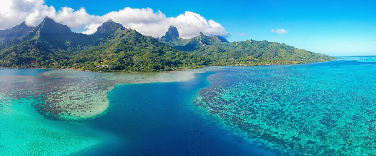 A tropical island with clear turquoise waters, lush green mountains, and a small settlement.
