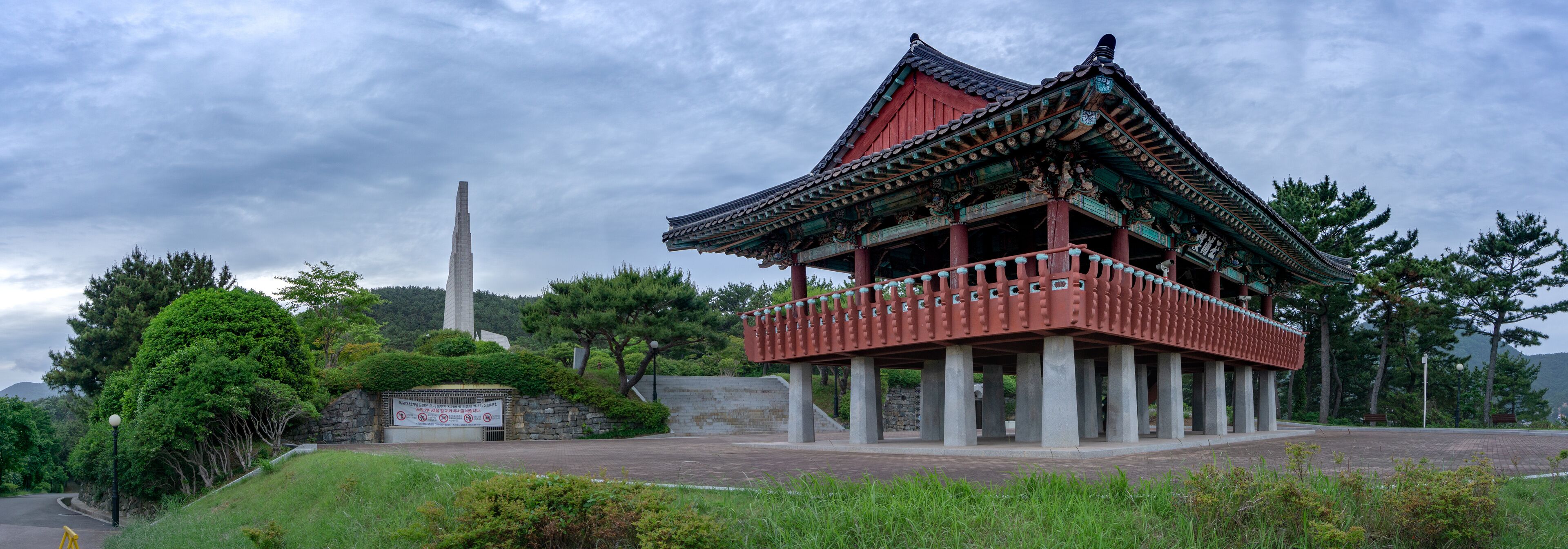 A traditional Korean pavilion with a stone monument in the background.