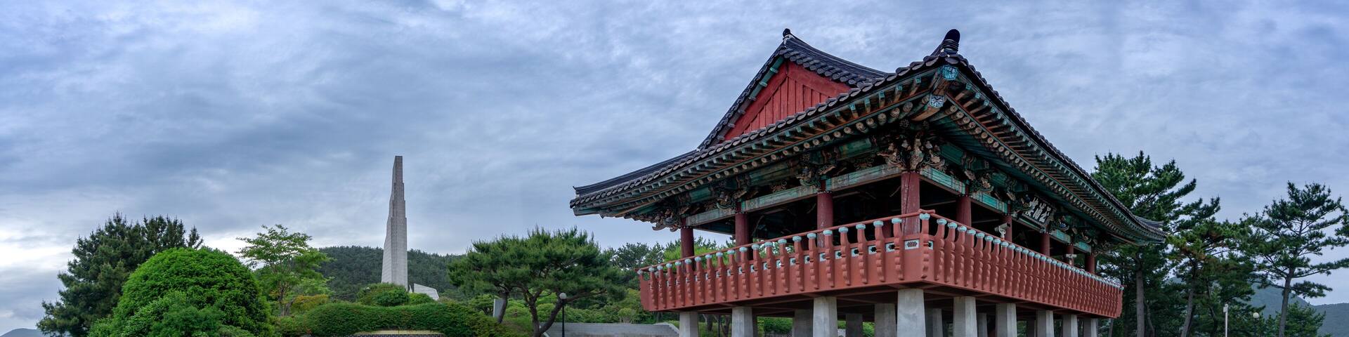 A traditional Korean pavilion with a stone monument in the background.