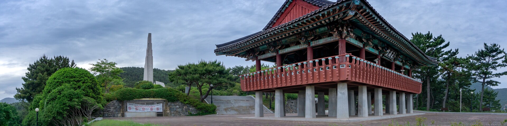 A traditional Korean pavilion with a stone monument in the background.