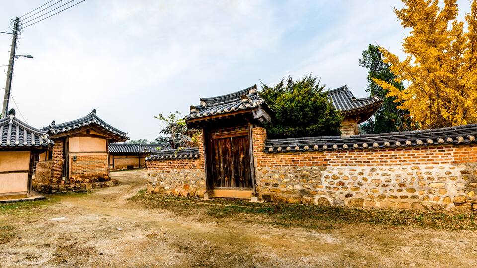 A traditional Korean village with stone walls, tiled roofs, and a dirt path.