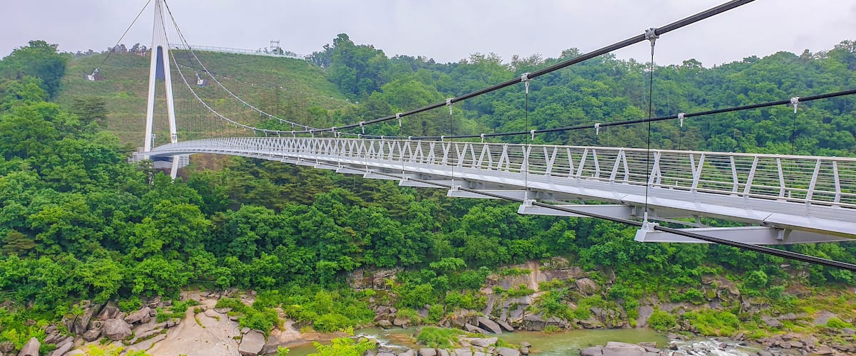 A suspension bridge over a river with a forested hillside in the background.