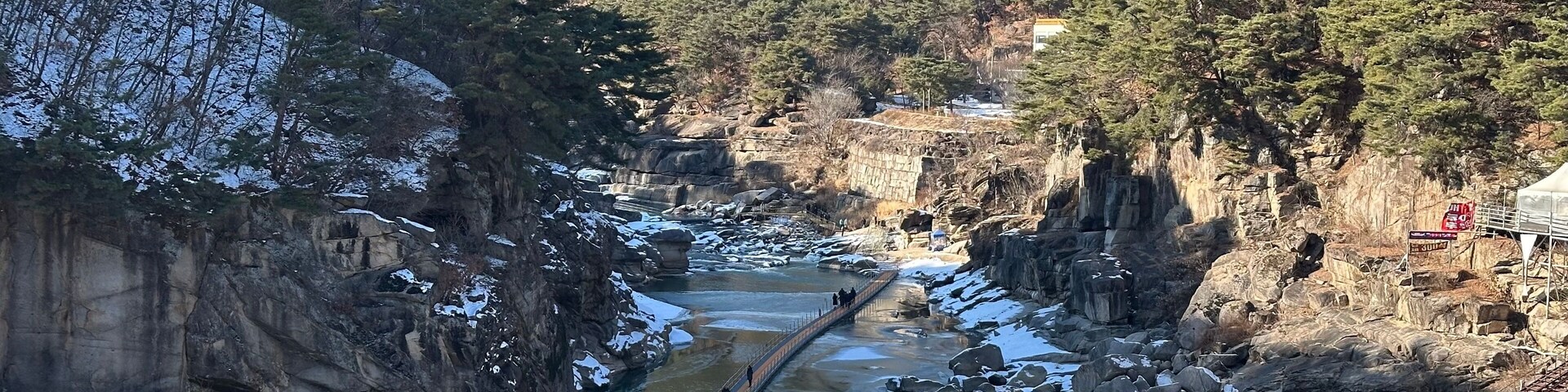 Un río serpentea por un cañón rocoso, con parches de nieve en el suelo y árboles a lo largo de las orillas.